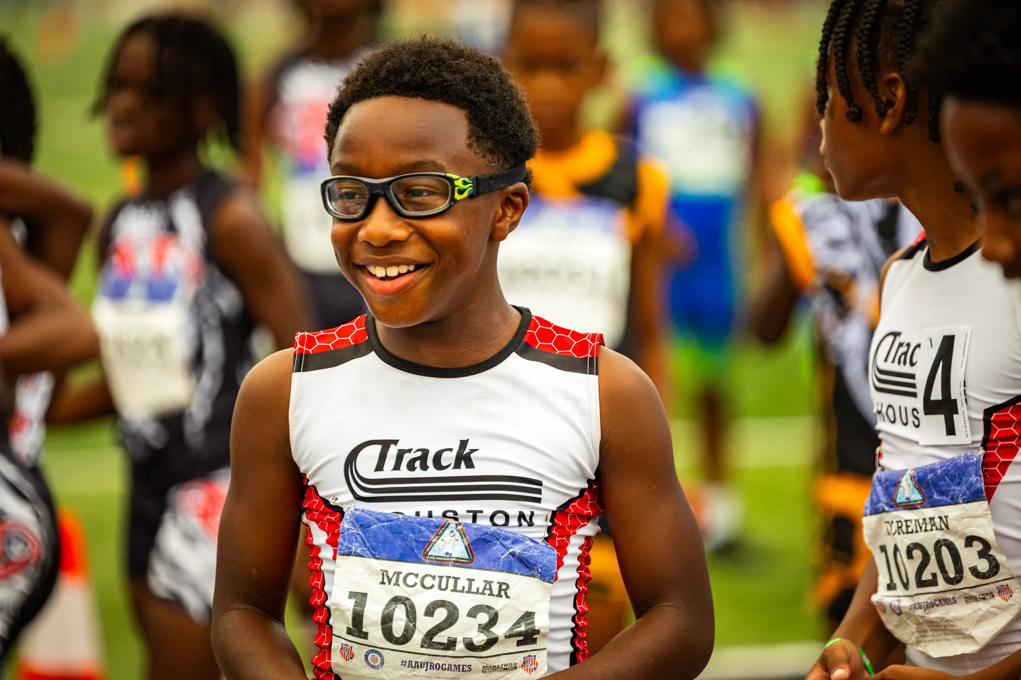 A young Track Houston athlete in goggles grins on the infield before his race.